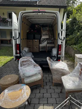 Gartenmöbel in Schutzfolie vor dem beladenen Transporter